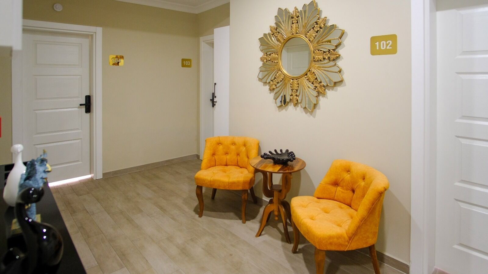 Una habitación con dos sillones amarillos, una mesita redonda y un espejo decorativo en la pared.