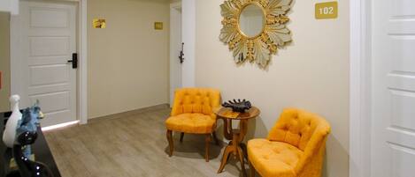 Una habitación con dos sillones amarillos, una mesita redonda y un espejo decorativo en la pared.