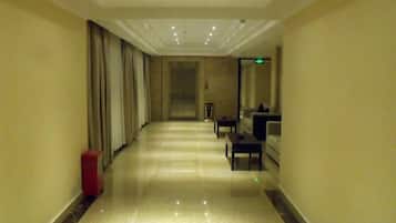 A hotel corridor with a red suitcase, a reception desk, and a seating area.