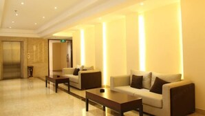 A lobby with two sofas and a coffee table, a reception desk, and a marble floor. - Xin Haiyi Hotel (Kaiping)