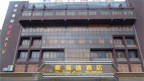 A hotel with a modern facade, multiple floors, and a prominent entrance with a sign. - Xin Haiyi Hotel (Kaiping)