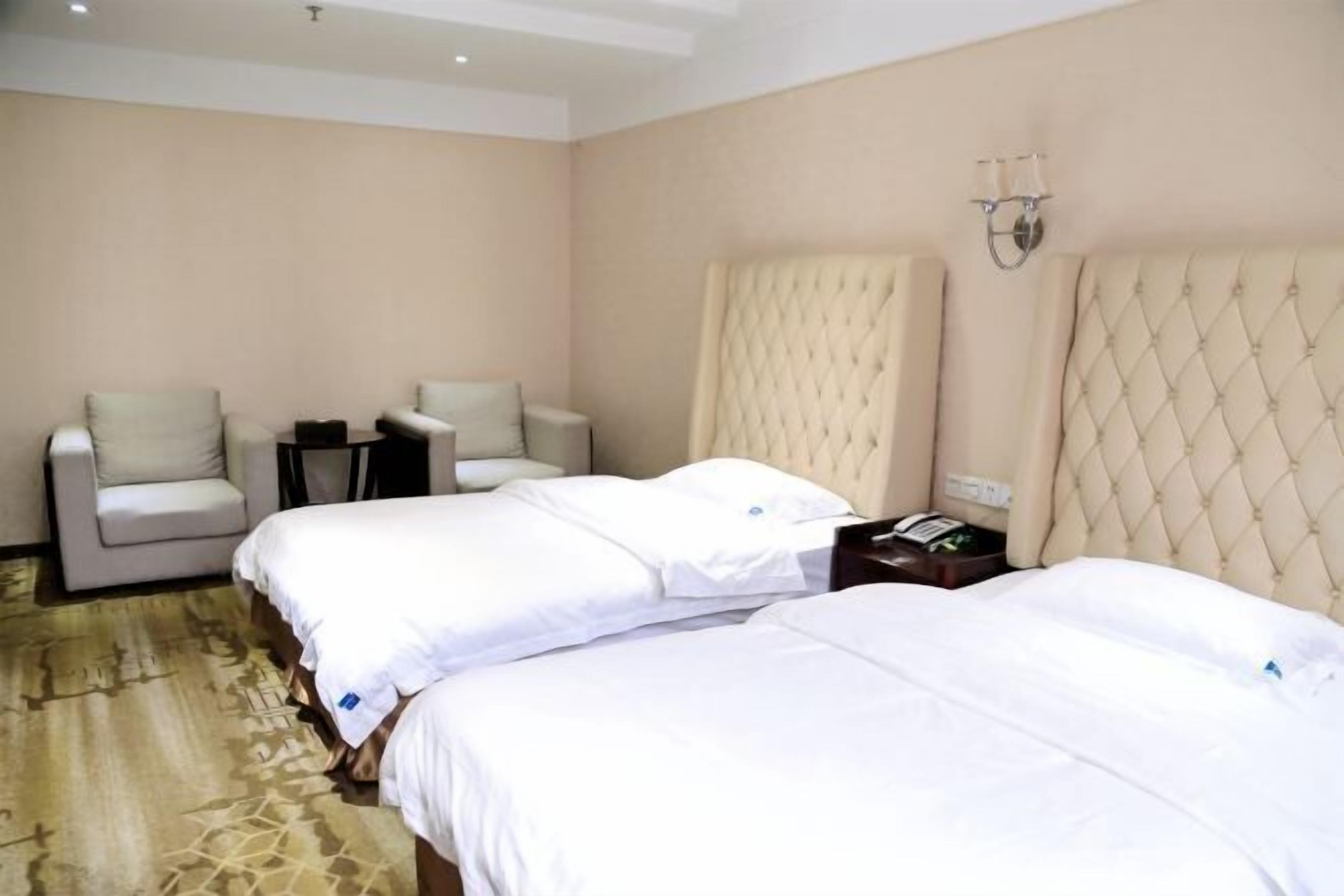 A hotel room with two beds, a small table, and a chair.