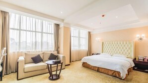 A hotel room with a bed, a sofa, a small table, and large windows. - Xin Haiyi Hotel (Kaiping)