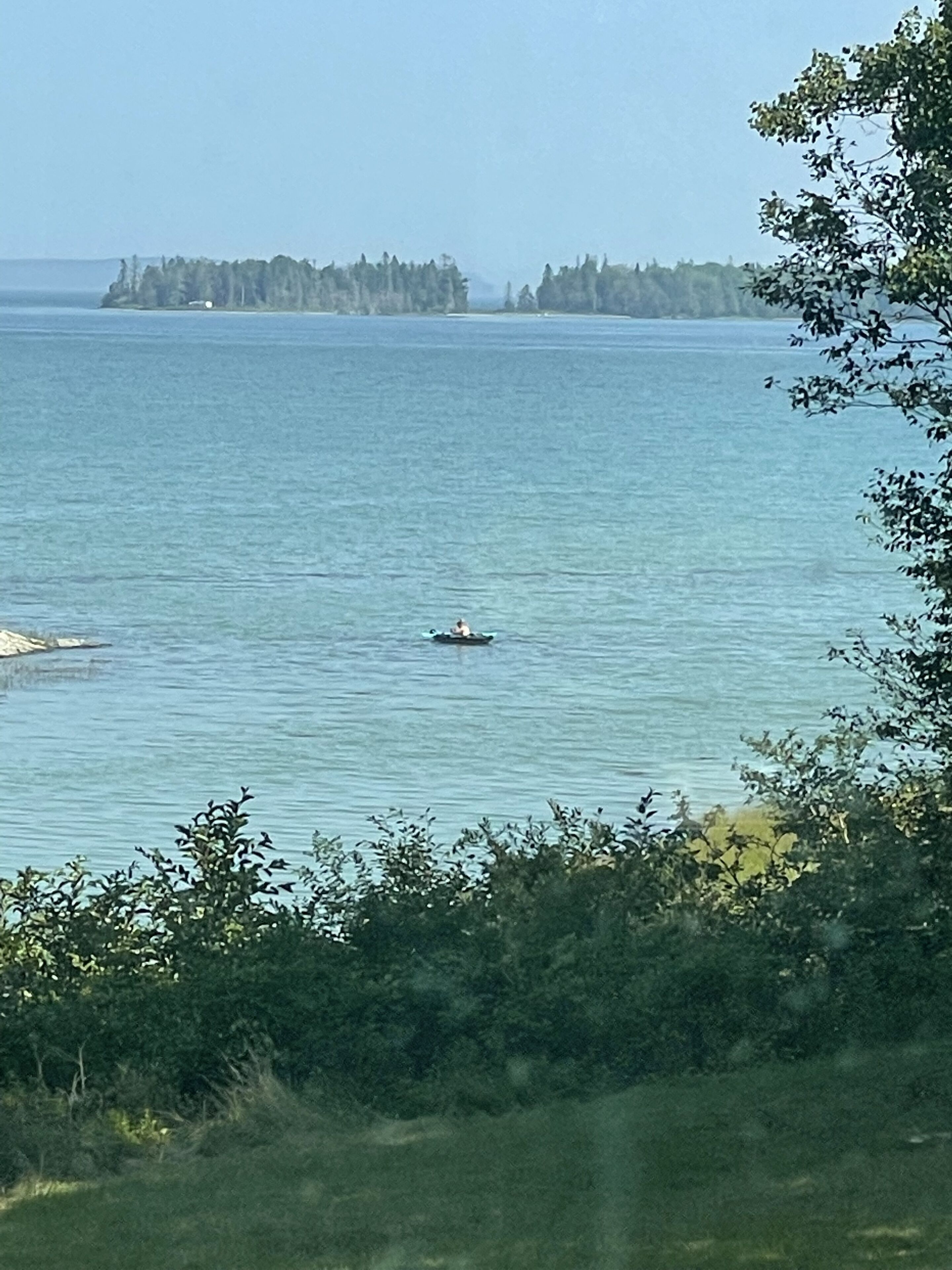A view of a calm body of water with a small boat in the distance, surrounded by dense greenery and a forested island.
