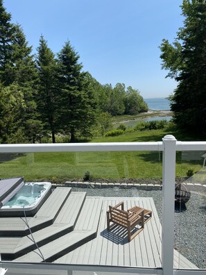 Une terrasse dotée d’un jacuzzi, de sièges en bois et offrant une vue sur un plan d’eau et des arbres.