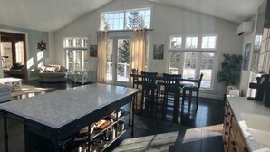 A spacious kitchen with a large island, dining area with chairs, and a view of the outdoors through large windows.