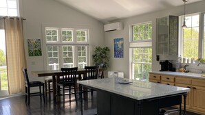 A spacious kitchen with a central island, large windows, and a dining area with chairs.