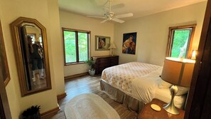 Ein Schlafzimmer mit einem Bett, einem Schminktisch, einem Spiegel, einem Deckenventilator und Fenstern.