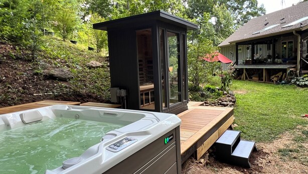 Een bubbelbad met een houten terras, een glazen constructie en een tuin met een houten terras en een huis op de achtergrond.