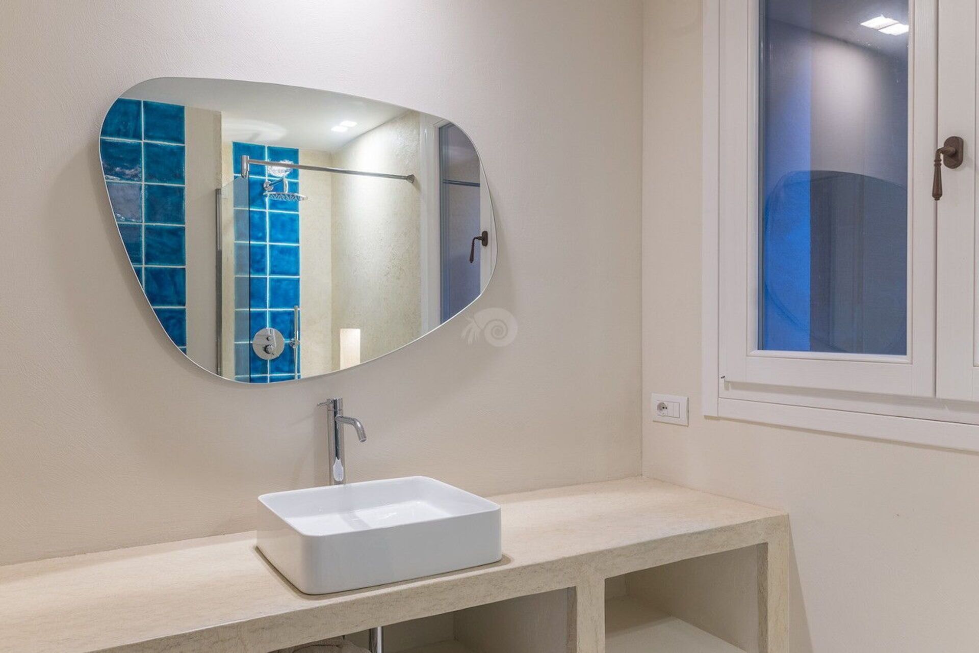 A bathroom with a white sink, a large oval mirror, and a shower with blue tiles.