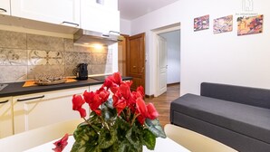 Et moderne køkken med kaffemaskine, et spisebord med en vase med røde blomster, og en grå sofa i en opholdsstue.