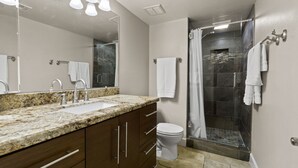 Une salle de bain moderne avec un lavabo sur un plan de travail en granit, des toilettes et une douche à parois de verre.