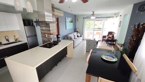 A modern kitchen with a central island, a dining area with a black table, and a living space with a sofa and chairs.
