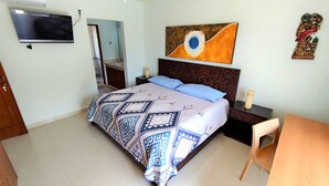 A bedroom with a bed, a TV mounted on the wall, a nightstand, a chair, and a table.