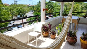 A private balcony with a hammock, potted plants, a table, and chairs.