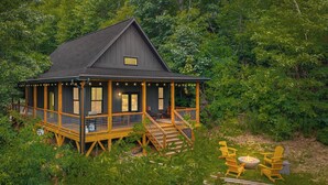 Une cabane dotée d’un porche, d’une terrasse en bois et d’un espace aménagé pour faire un feu de camp.