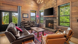 Un intérieur de chalet chaleureux avec des canapés en cuir, une cheminée et de grandes fenêtres donnant sur le paysage extérieur.