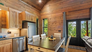 L’intérieur d’un chalet en bois comprend une cuisine, un coin repas et un canapé placé près d’une grande fenêtre.