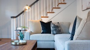 Una sala de estar moderna con un sofá gris, una mesa de centro de madera y una escalera con barandillas blancas.