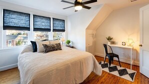 Un dormitorio con cama, ventilador de techo, escritorio con silla y vista al exterior.