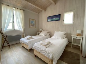 Une chambre avec deux lits, du linge de lit blanc, un tableau au mur et une fenêtre avec des rideaux.