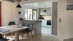 Una cocina moderna con armarios blancos, un comedor con mesa y sillas de madera, y vistas al exterior a través de una ventana.