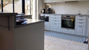 Una cocina moderna con armarios blancos, horno empotrado y cafetera.