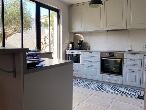 A modern kitchen with white cabinets, a built-in oven, and a coffee maker. - Charming Ile de Ré house, 2 steps from beaches and golf course. (Saint-Clément-des-Baleines)