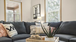 A modern living room with a grey sectional sofa, decorative pillows, a small table with a plant, and a framed artwork on the wall.