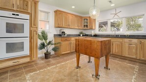 A kitchen with wooden cabinets, a double oven, a central island, and a hanging light fixture.