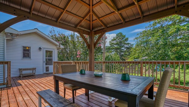 A wooden deck with a table and chairs, a covered area, and a view of a house and trees.