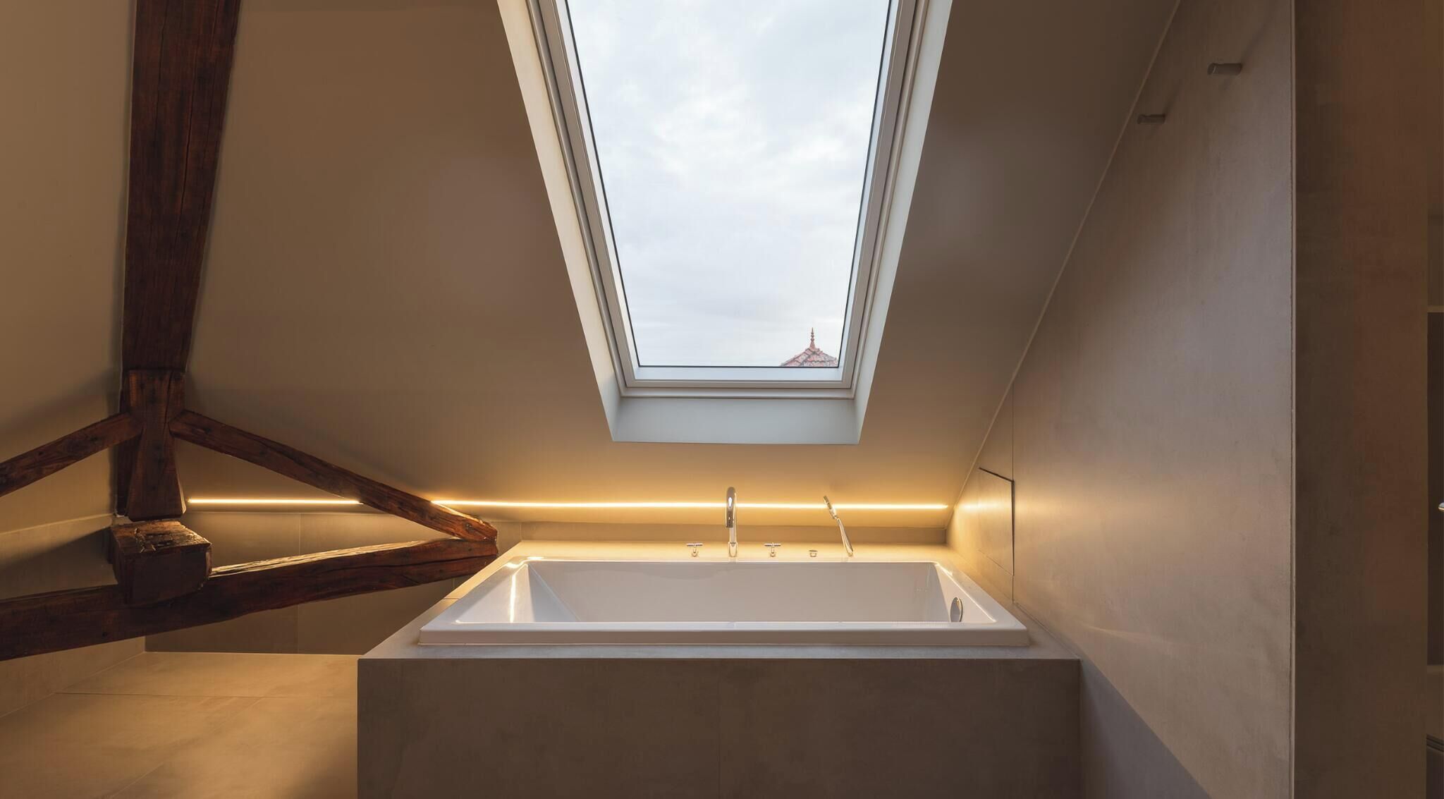 A skylight above a bathtub in a modern bathroom with wooden beams and a view of the sky.