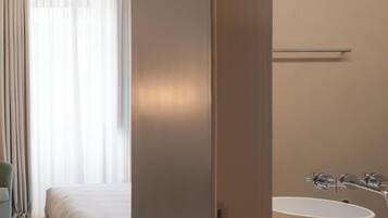 A hotel room with a bed, a large window with curtains, and a bathroom with a sink and mirror.