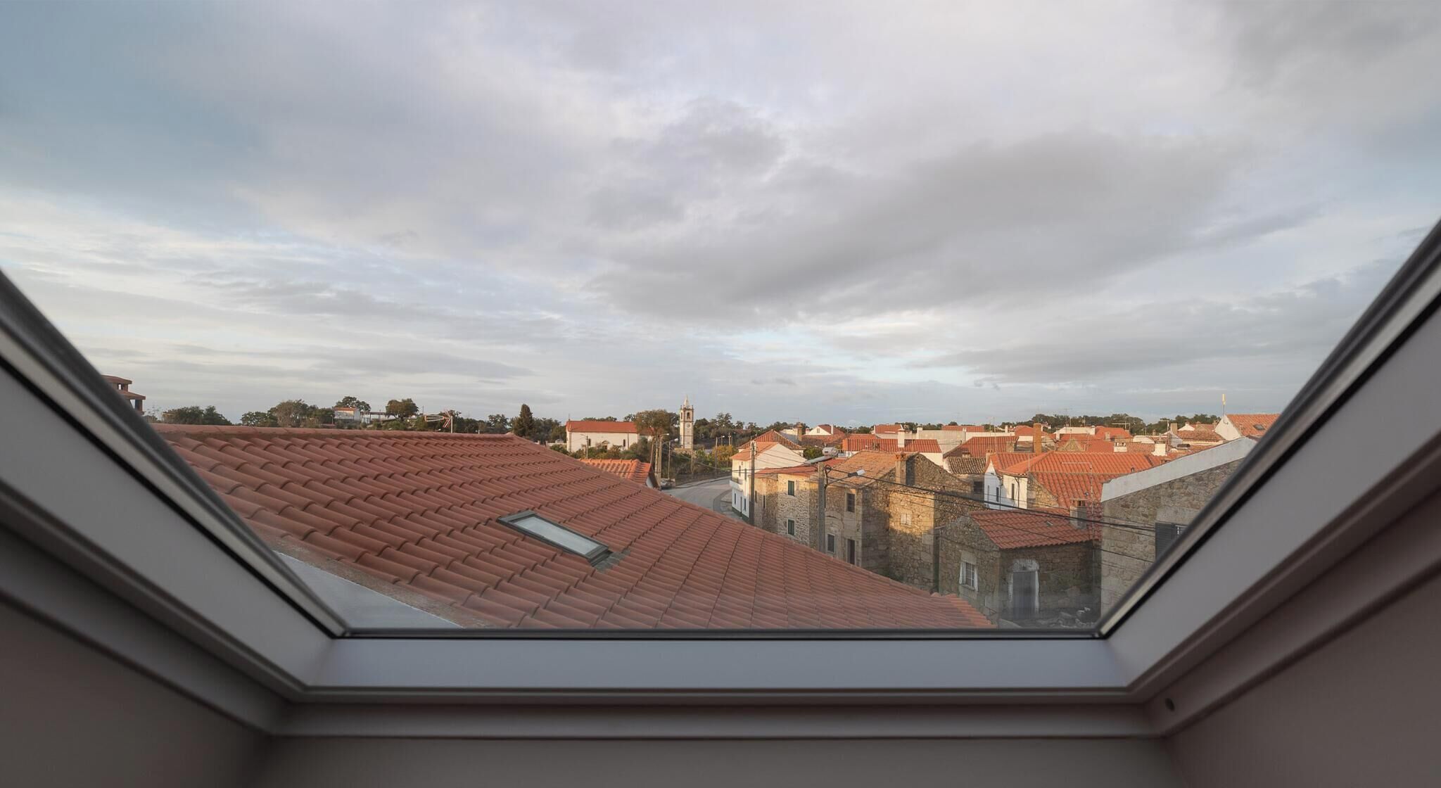 A view from a skylight of a residential area with red-tiled roofs and a mix of stone and brick buildings.