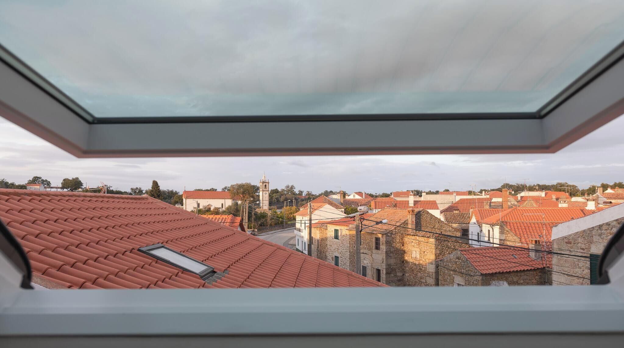Vista desde un tragaluz de un pueblo con tejados rojos y una imponente torre del reloj.