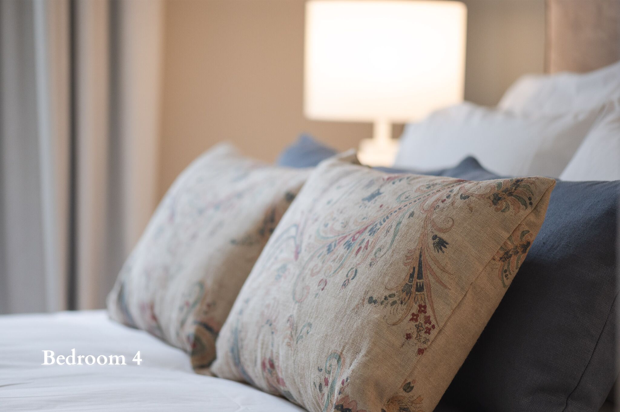 A bedroom with a bed, pillows, and a lamp in the background.