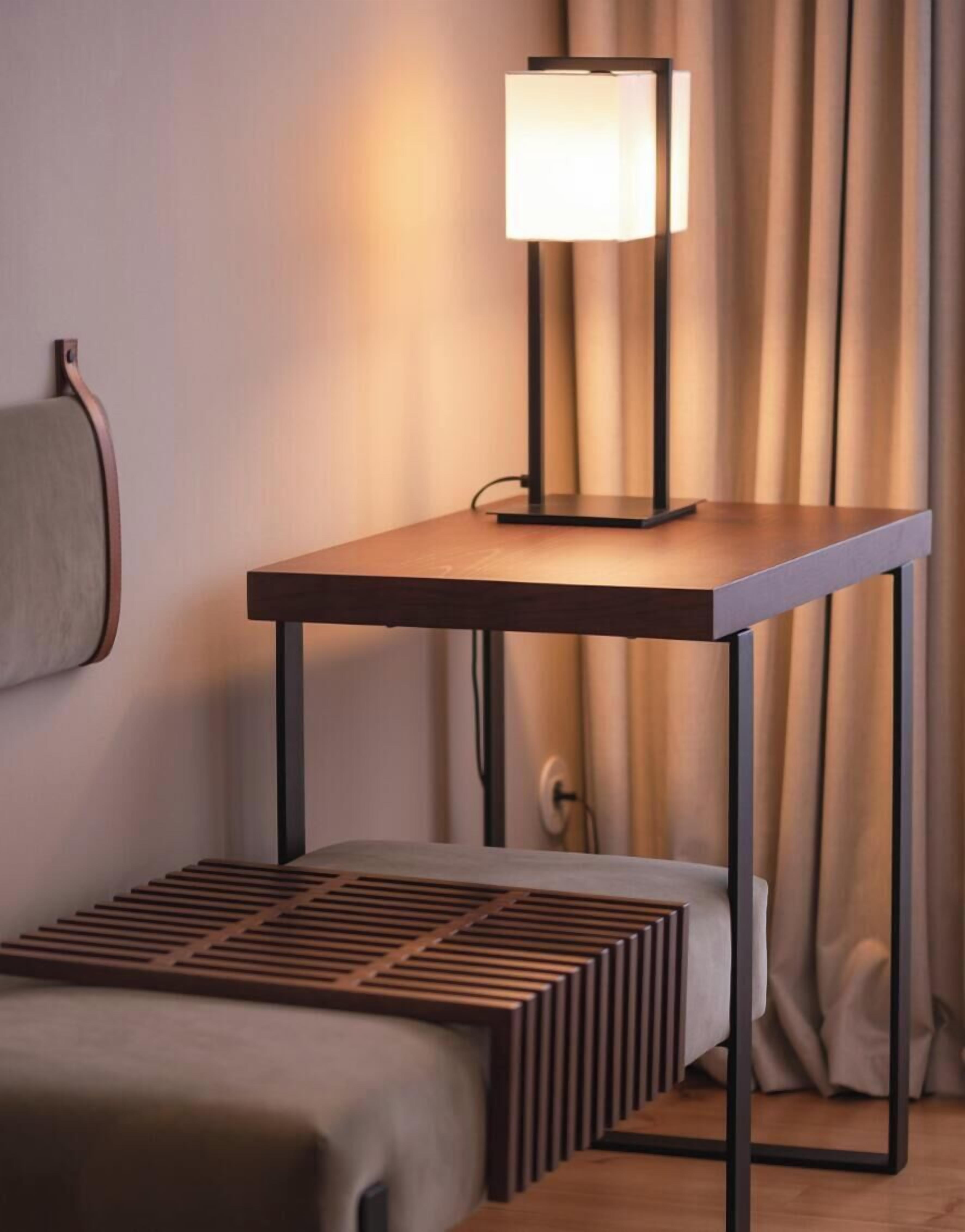 Une chambre moderne avec une table de chevet, une lampe, un lit et un rideau.