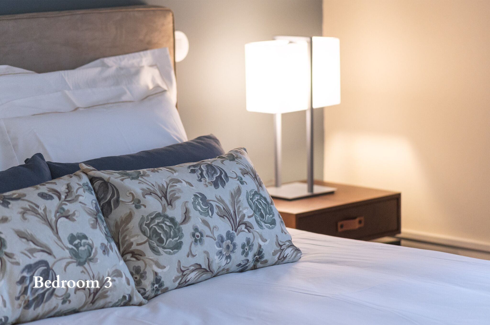 A neatly made bed with floral-patterned pillows and a bedside table with a lamp.