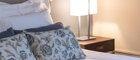 A neatly made bed with floral-patterned pillows and a bedside table with a lamp.