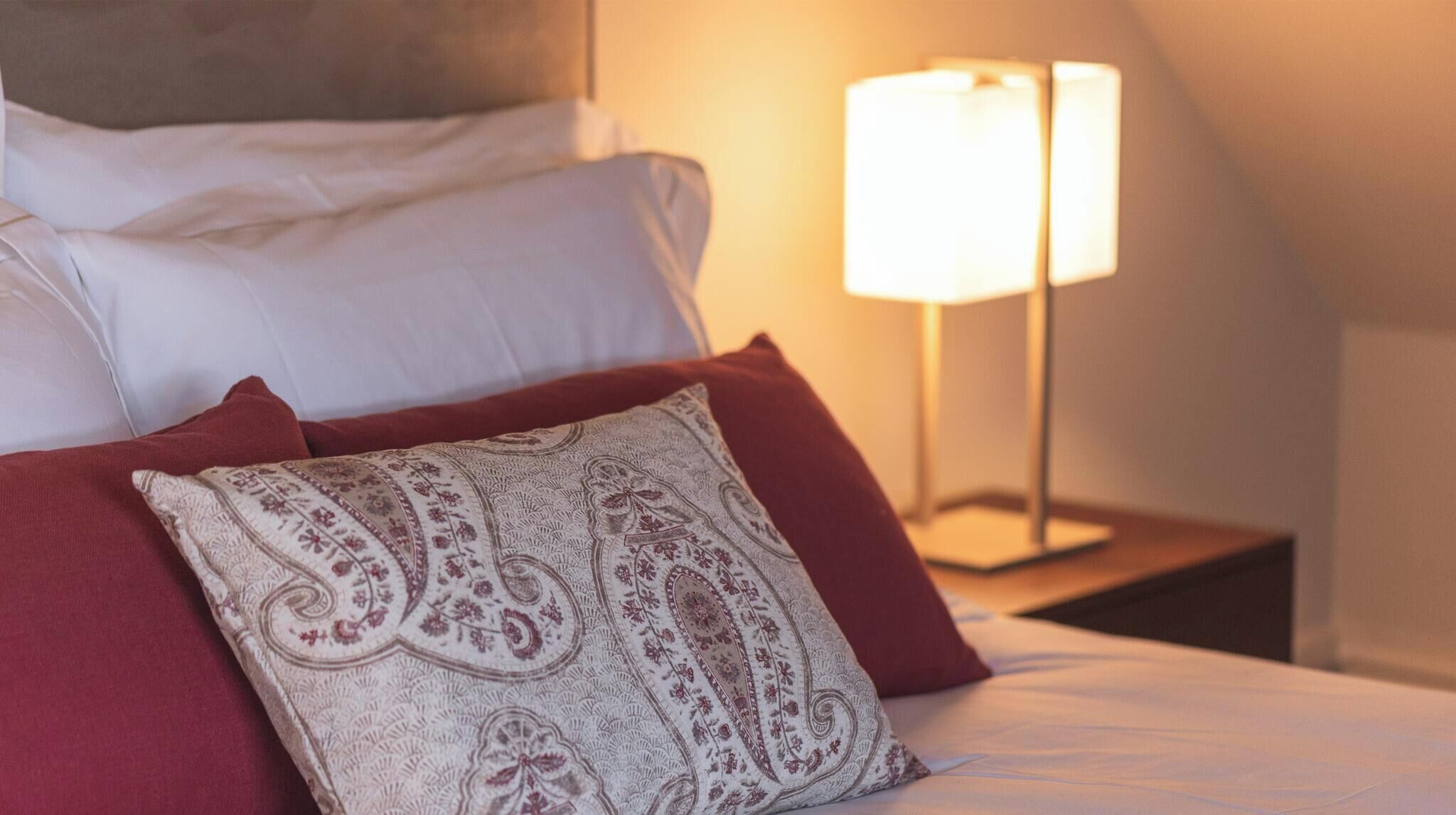 Una cama bien hecha con sábanas blancas y un cojín decorativo con estampado de cachemir.
