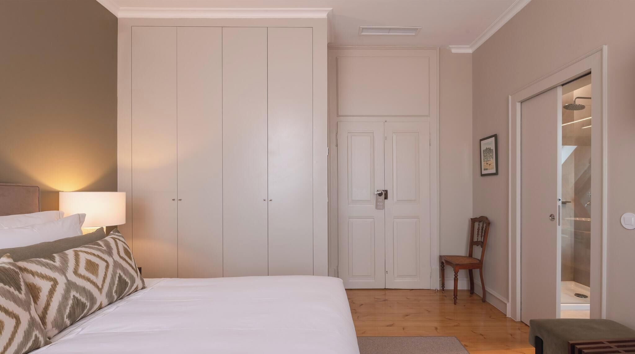 Een slaapkamer met een bed, nachtkastje, stoel en kledingkast.
