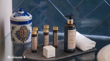 Un baño con pared de azulejos azules, un recipiente de cerámica blanco con tapa azul y distintos artículos de aseo, incluyendo una botella de champú, una botella de acondicionador y un gorro de ducha.