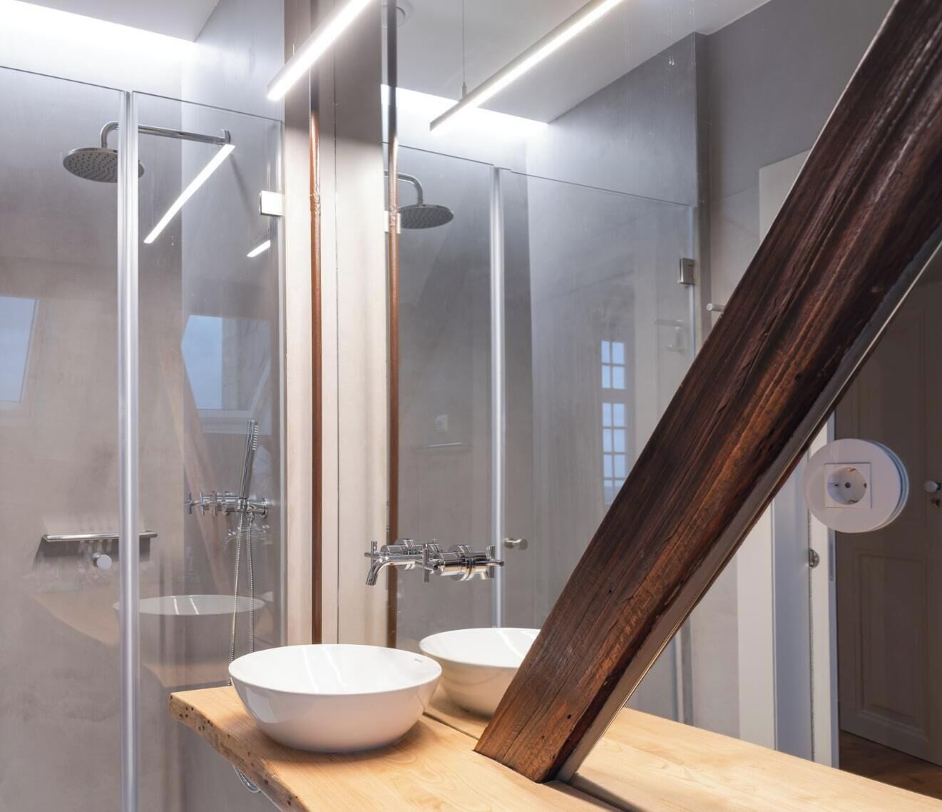 A modern bathroom with a glass shower enclosure, two sinks, and a wooden countertop.