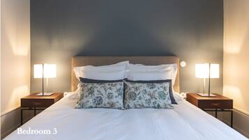 A neatly made bed with floral pillows in a bedroom with two bedside lamps and a nightstand.