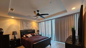 Un dormitorio moderno con cama, ventilador de techo, televisor y ventana con cortinas.