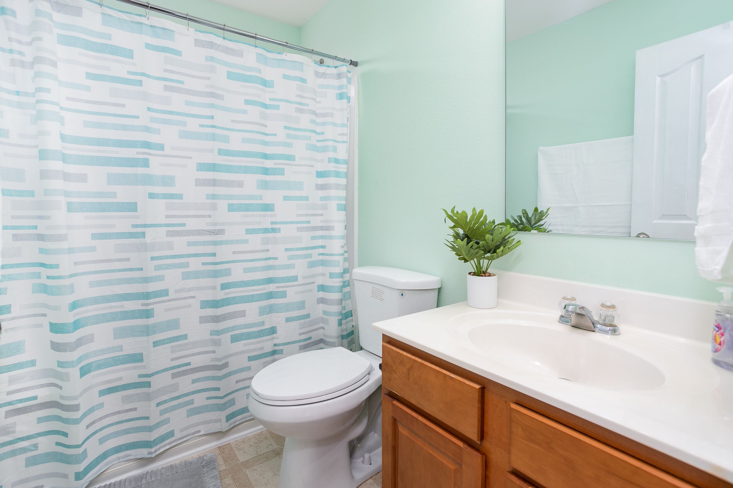 A bathroom with a shower curtain, toilet, sink, and cabinets.