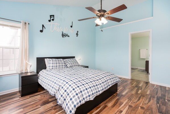 A bedroom with a bed, a nightstand, a ceiling fan, and a wall with musical notes and text. - Modern, Relaxing, Peaceful home near Furniture Market and High Point University (High Point)