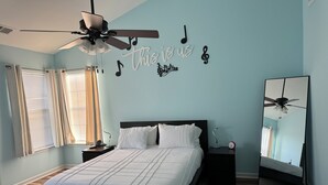 Ein Schlafzimmer mit Bett, Deckenventilator, Nachttisch, Spiegel und einer Wand mit Noten und Text.