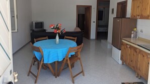Eine kompakte Küche mit Essbereich, inklusive rundem Tisch mit Stühlen, einem kleinen Kühlschrank, Holzschränken und einem Fernseher in der Ecke.