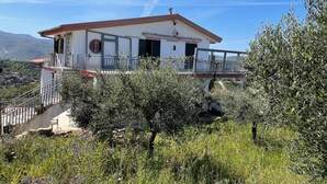 Ein zweigeschossiges Haus mit Balkon, umgeben von Olivenbäumen und einer Berglandschaft.